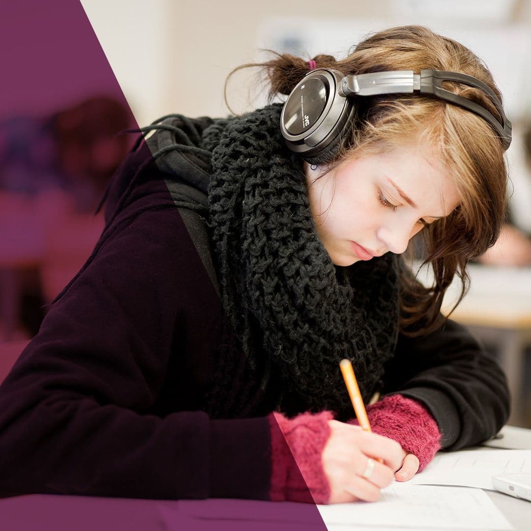 Kvinna som sitter med hörlurar och skriver med penna och papper